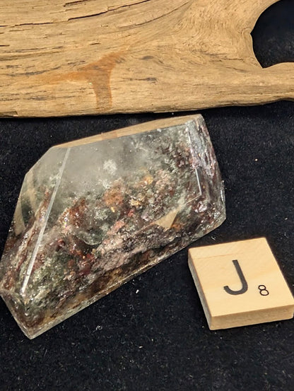 Exact piece Garden Quartz faceted freeform, Variant J8, characterized by a thick, multi-colored base layer of green, red, and silver-toned mineral deposits.