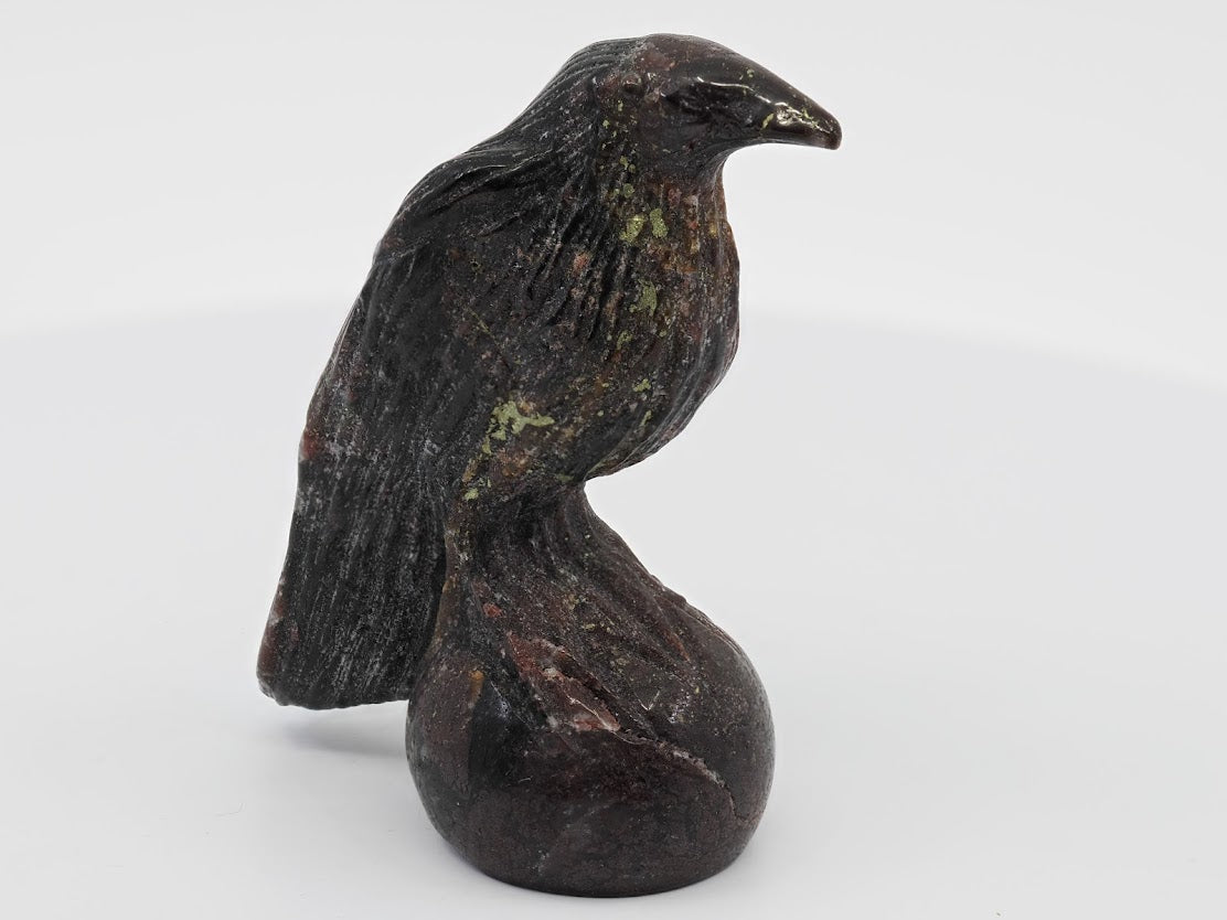 Three-quarter view of a dark burgundy Garnet raven totem perched on a sphere, highlighting natural mineral texture.
