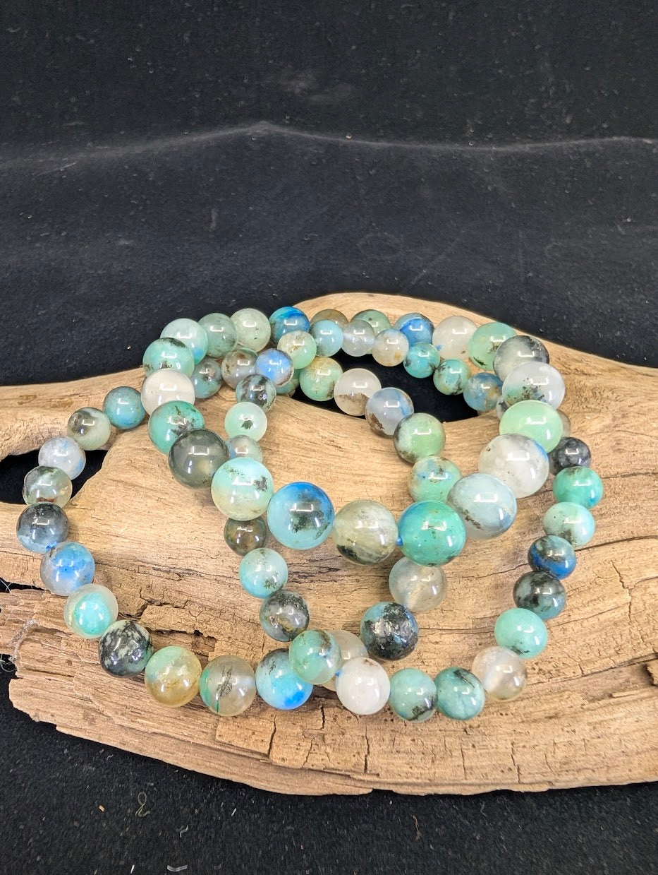 Stacked 6mm, 7mm, and 9mm Gem Silica (Silicified Chrysocolla) bracelets on driftwood showing varying bead sizes and vibrant teal color.