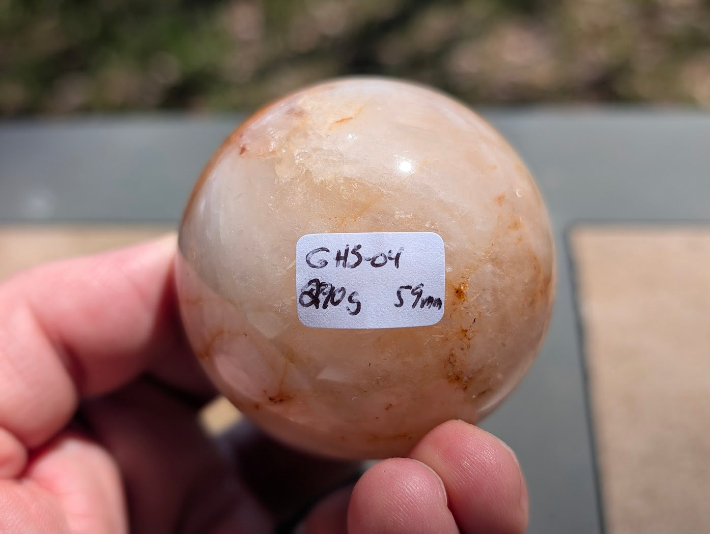 Hand holding Golden Healer quartz sphere GHS-04 showing scale and physical weight label.