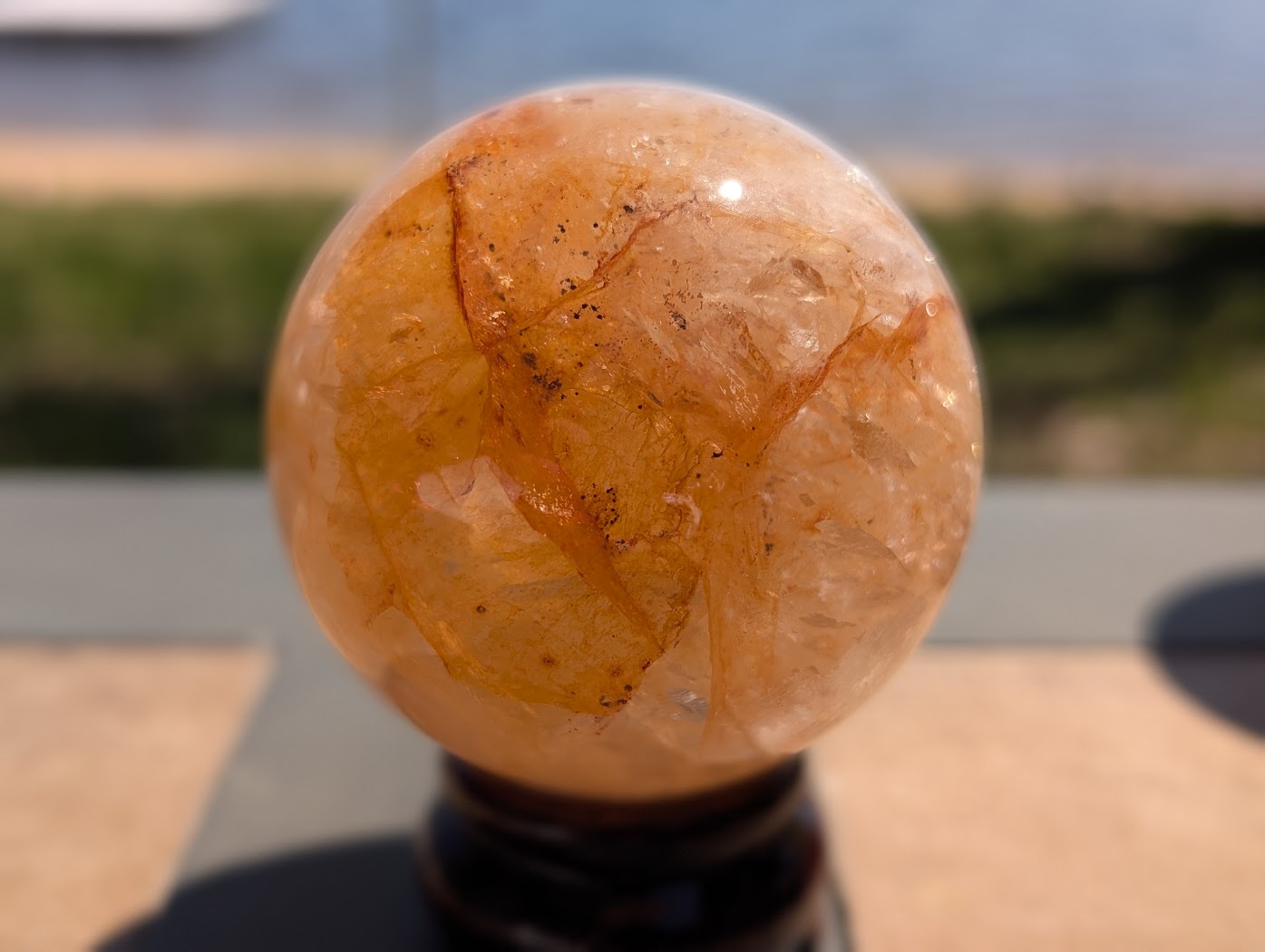 Close-up of Golden Healer quartz sphere GHS-05 highlighting natural internal cleavage planes and warm golden fire.