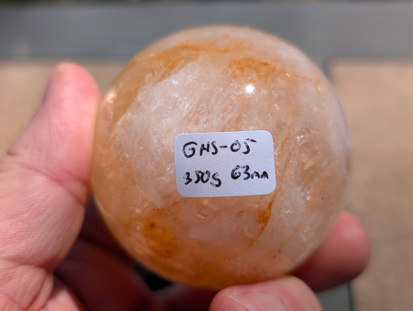 Hand holding Golden Healer quartz sphere GHS-05 showing scale and physical weight label.