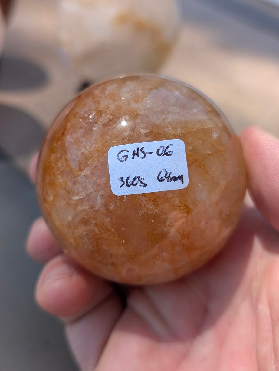 Hand holding Golden Healer quartz sphere GHS-06 showing scale and physical weight label.