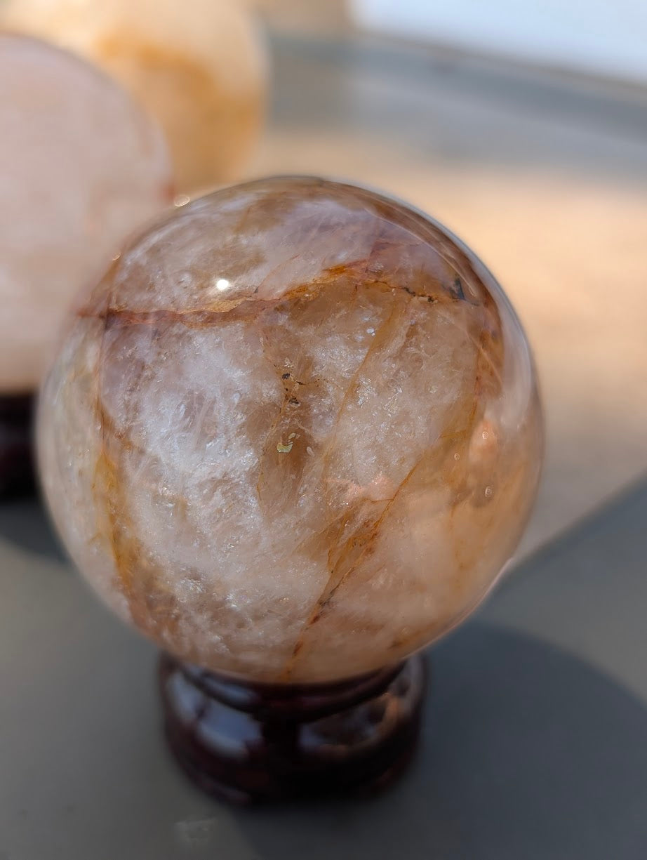 Exact-piece Golden Healer (ferruginous quartz) sphere from Brazil. 65mm variant GHS-03 offering a balanced mix of transparent windows and opaque iron-oxide banding.