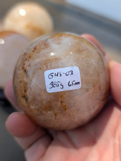 Hand holding Golden Healer quartz sphere GHS-03 showing scale and physical weight label.