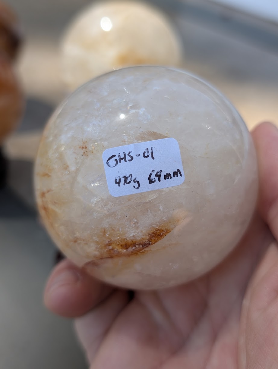 Hand holding Golden Healer quartz sphere GHS-01 showing scale and physical weight label.
