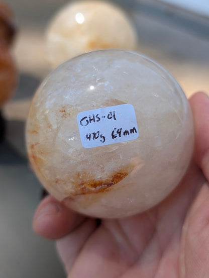 Hand holding Golden Healer quartz sphere GHS-01 showing scale and physical weight label.