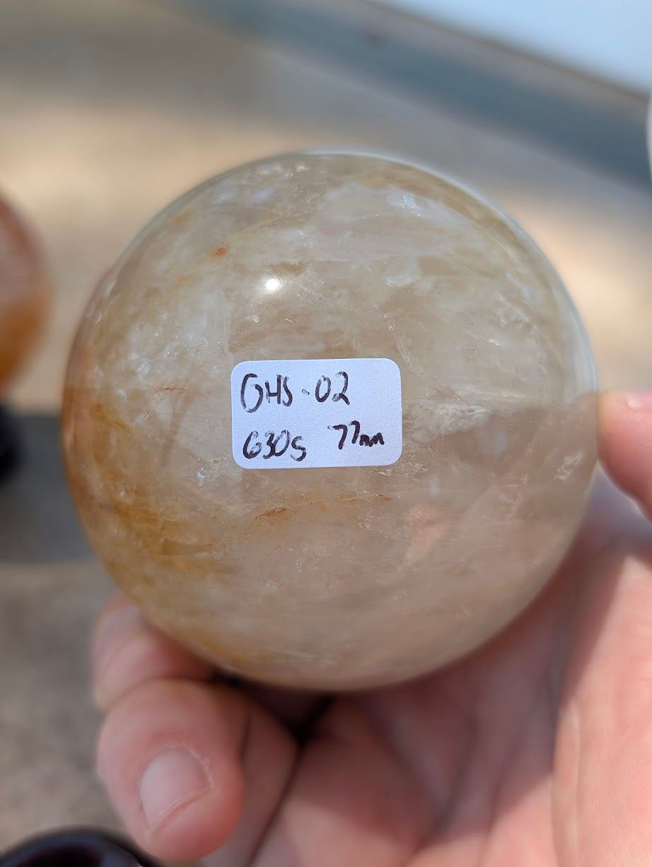 Hand holding large Golden Healer quartz sphere GHS-02 showing scale and physical weight label.