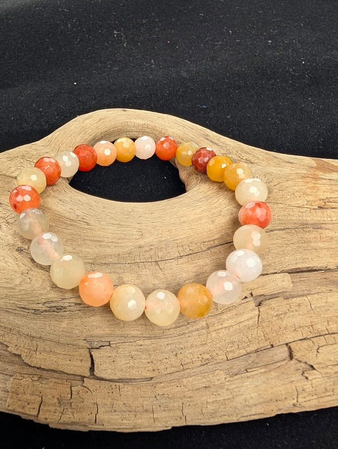 8mm faceted Golden Jade beaded stretch bracelet resting on a driftwood display, showing warm peach and yellow colouration.