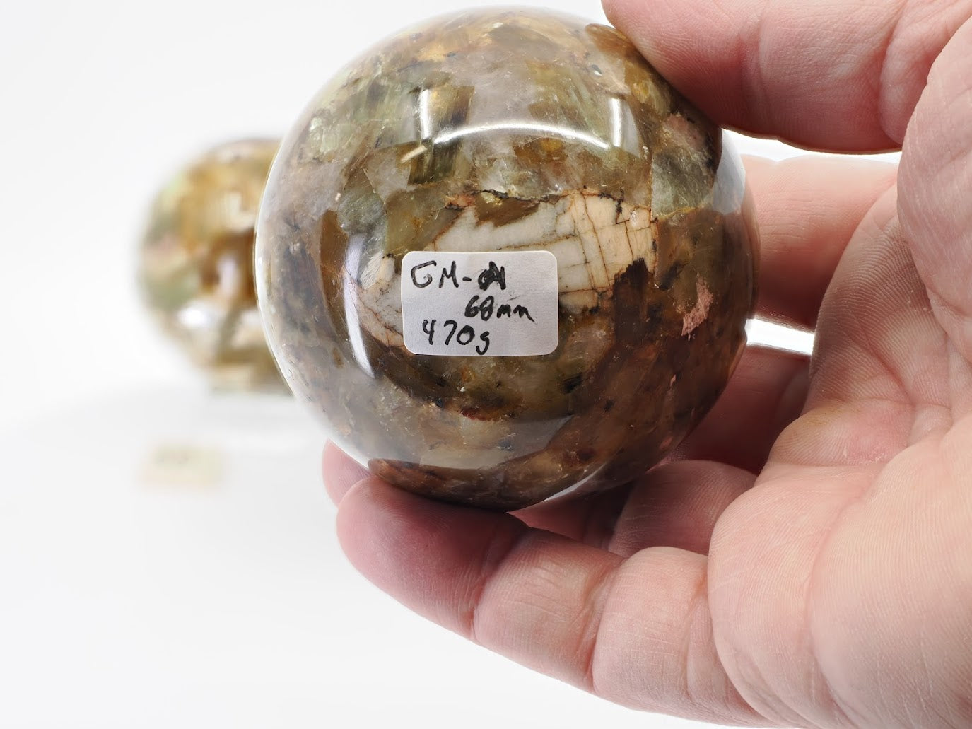 Close-up of Golden Mica sphere A being held to show 68mm size and 470g weight label on a polished mineral surface.