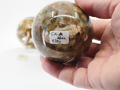 Close-up of Golden Mica sphere A being held to show 68mm size and 470g weight label on a polished mineral surface.