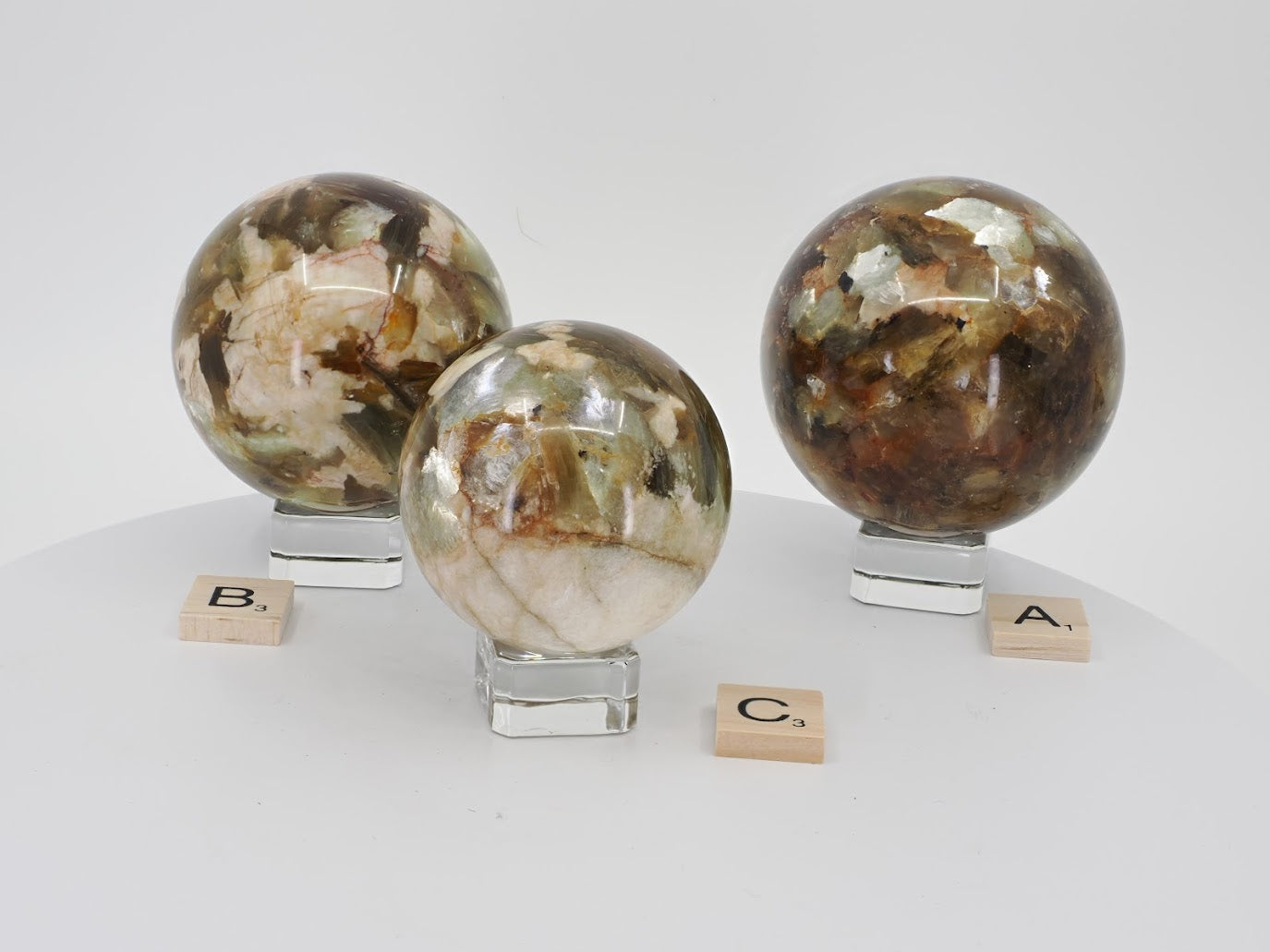 Group display of three premium Golden Mica spheres (Phlogopite) on glass stands showing variations in size and color.