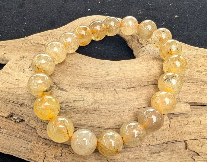10mm polished Golden Rutilated Quartz beaded stretch bracelet resting on a driftwood display, showing translucent stones with golden rutile inclusions.