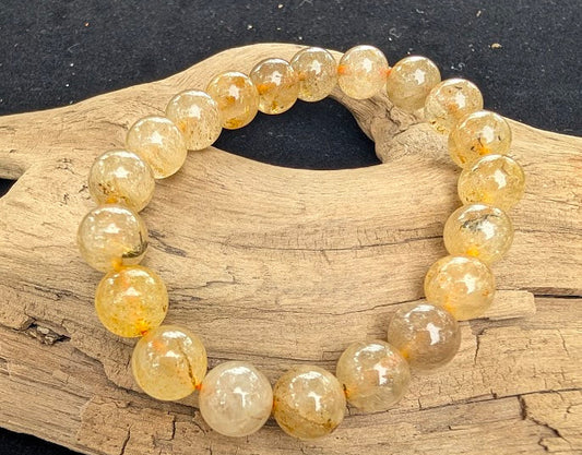 10mm polished Golden Rutilated Quartz beaded stretch bracelet resting on a driftwood display, showing translucent stones with golden rutile inclusions.