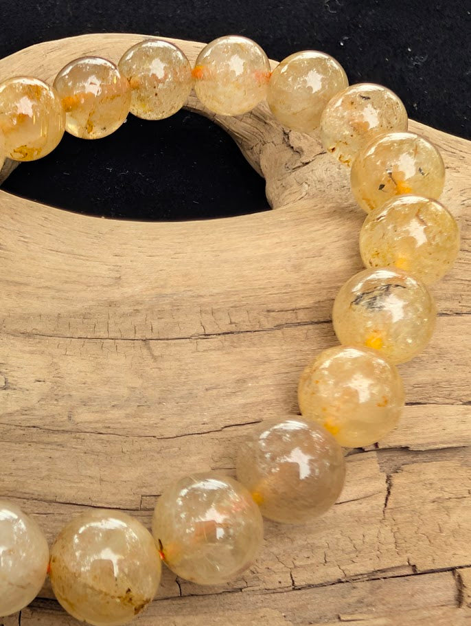 Macro close-up of 10mm polished Golden Rutilated Quartz beads highlighting the high-gloss finish and the internal metallic rutile needles.