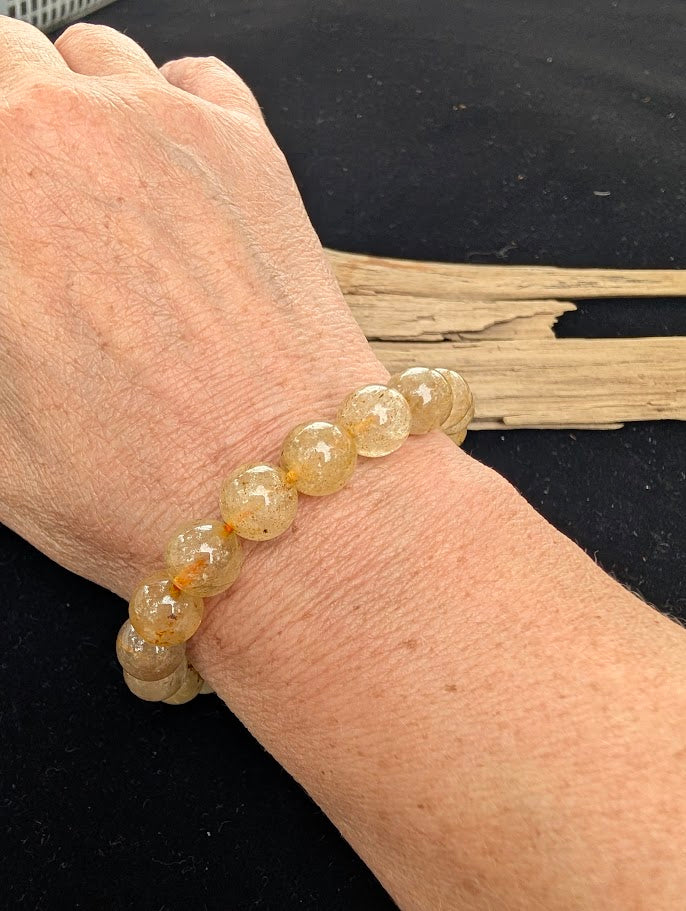 10mm polished Golden Rutilated Quartz beaded stretch bracelet worn on a wrist for size scale.
