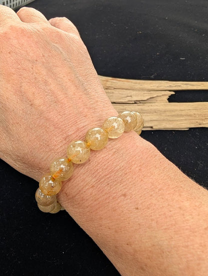10mm polished Golden Rutilated Quartz beaded stretch bracelet worn on a wrist for size scale.
