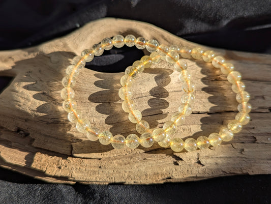 A 6mm Golden Rutilated Quartz round bead stretch bracelet positioned on a neutral presentation surface, demonstrating bead uniformity and natural golden rutile needle inclusions