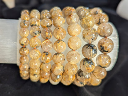 Macro detail of a Golden Rutilated Quartz bead from Brazil, emphasizing the glass-like polish and the intersecting acicular golden rutile crystals.