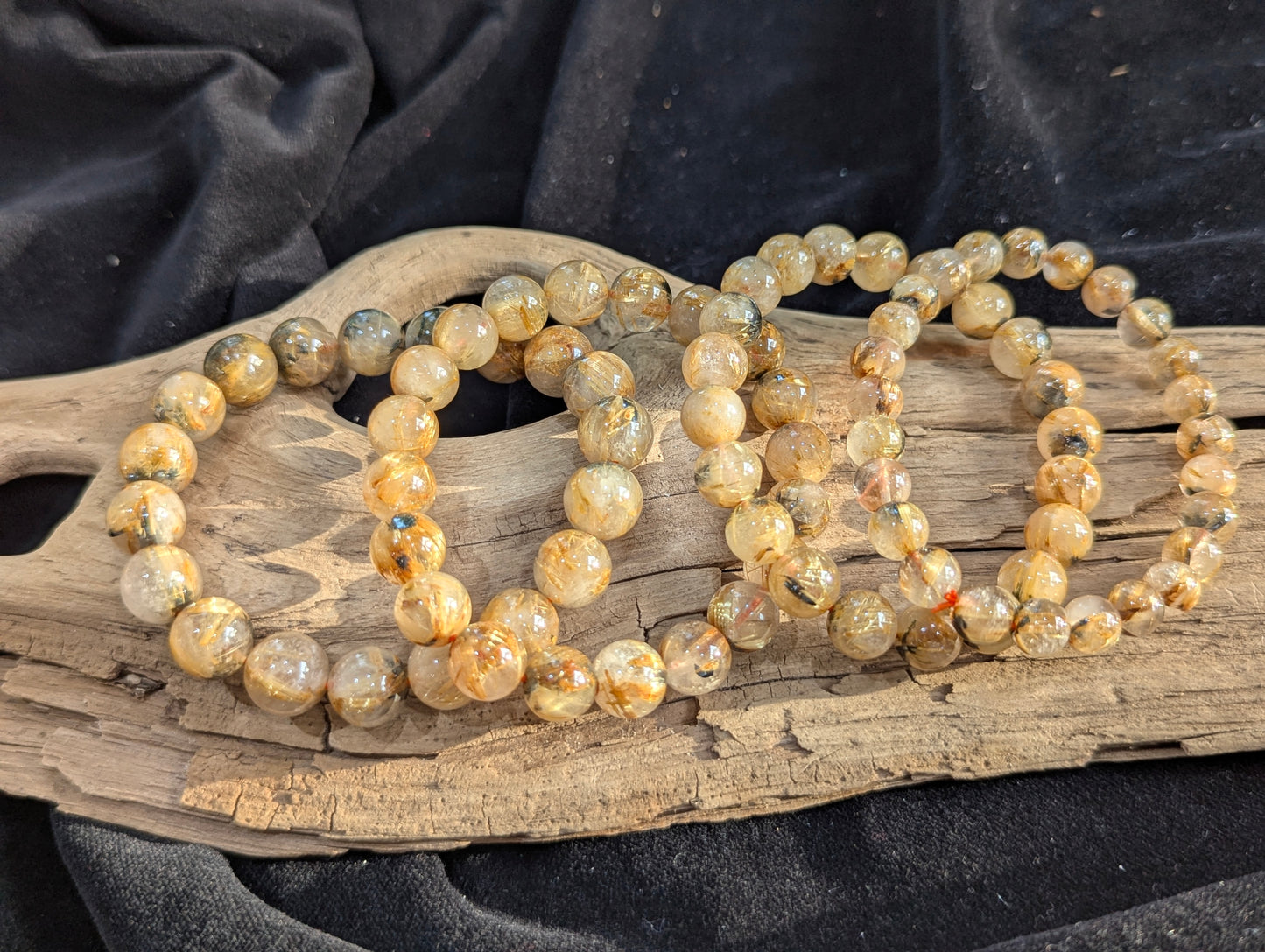 A collection of premium Golden Rutilated Quartz stretch bracelets from Brazil, ranging from 8mm to 13mm, showing high-clarity quartz and dense golden inclusions.