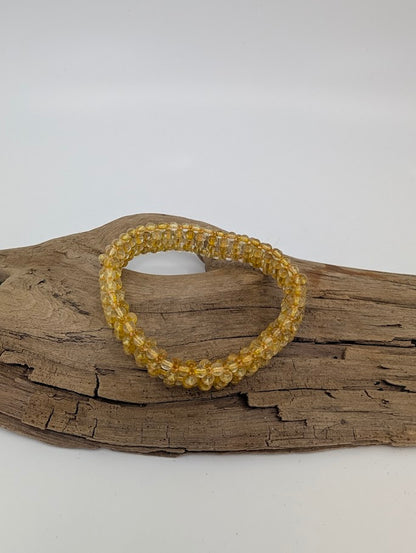 Golden Rutilated Quartz bracelet with golden rutile threads displayed on driftwood