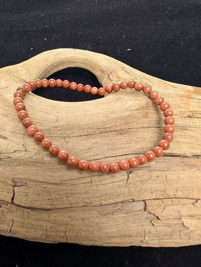 4mm polished Golden Sandstone beaded stretch bracelet resting on a driftwood display, showing a terracotta matrix with copper sparkle inclusions.