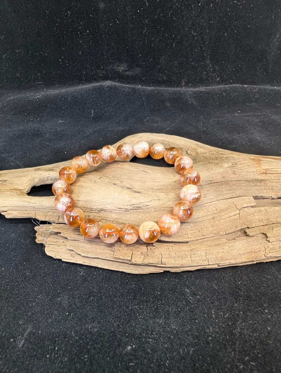 Natural Golden Sericite Phantom Quartz bracelet with 10mm polished beads displayed on natural driftwood.