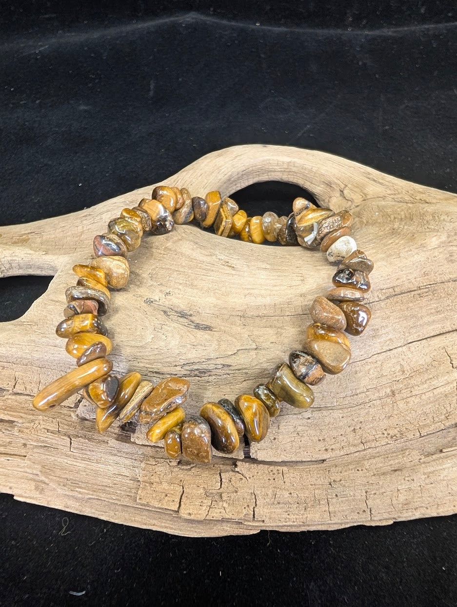 Natural Golden Tiger’s Eye chip bracelet with shimmering chatoyant mineral fragments on a driftwood display.