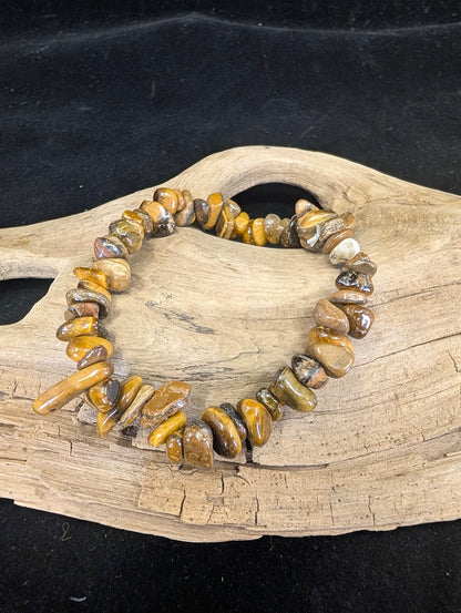Natural Golden Tiger’s Eye chip bracelet with shimmering chatoyant mineral fragments on a driftwood display.