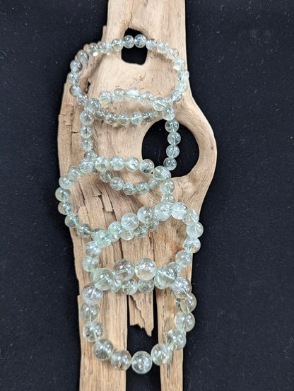 Assorted sizes of Green Amethyst (Prasiolite) Bracelets arranged vertically on a piece of driftwood