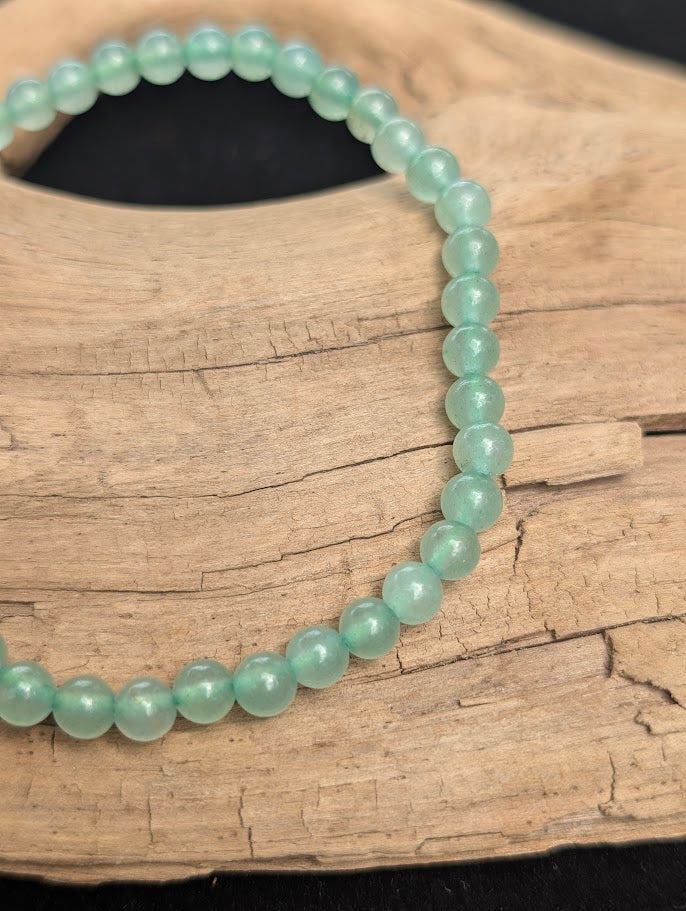 Macro view of polished 4mm Green Aventurine spherical beads on driftwood, highlighting the natural translucency and subtle internal fuchsite inclusions.