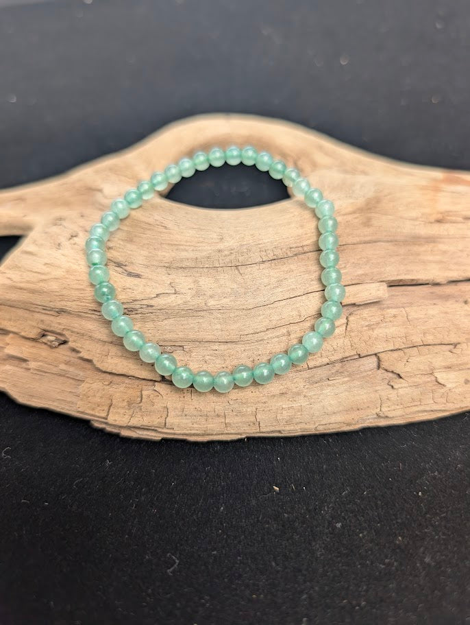 A 4mm Green Aventurine beaded bracelet resting on natural driftwood, displaying translucent, soft mint green quartz colours.