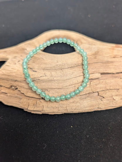 A 4mm Green Aventurine beaded bracelet resting on natural driftwood, displaying translucent, soft mint green quartz colours.