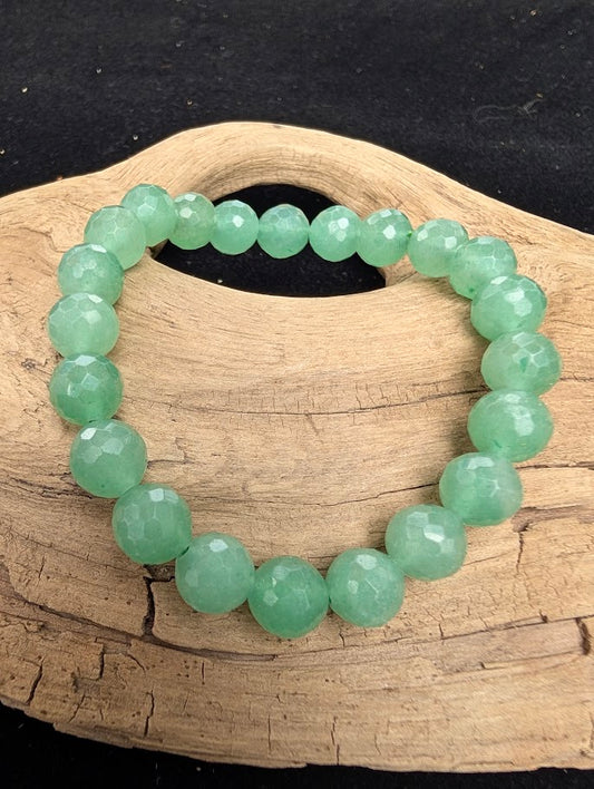 8mm faceted Green Aventurine beaded stretch bracelet resting on a driftwood display, showing vibrant emerald and mint green tones.