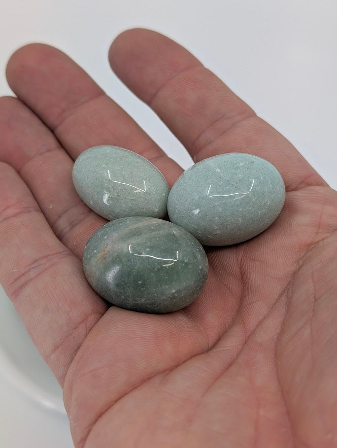 Hand holding Green Aventurine tumbled stones to show AA grade polish, color uniformity, and size scale
