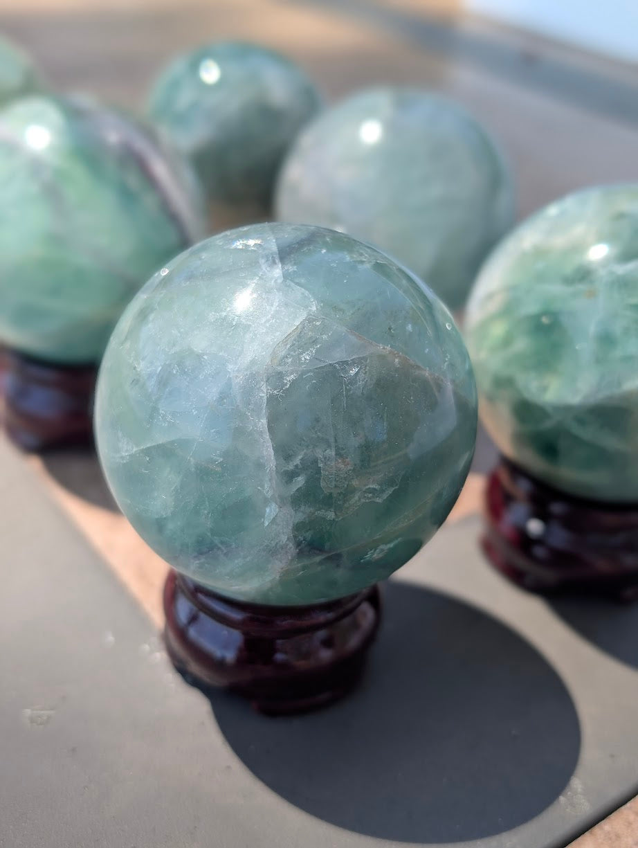 Close-up of a polished green fluorite sphere displaying internal cleavage planes, resting on a dark wood display stand.