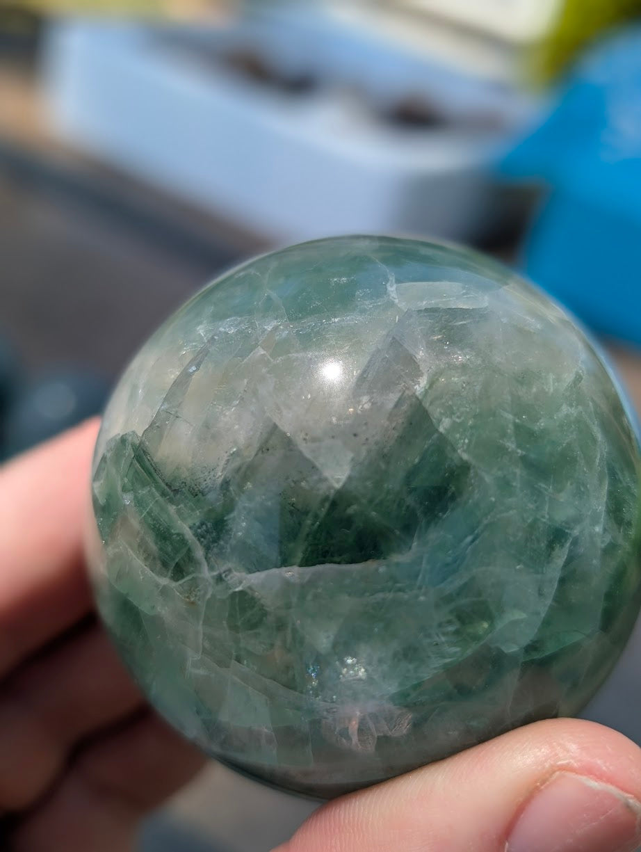 Close-up of a semi-translucent green fluorite sphere held in a hand, showcasing mint hues and structural clarity.