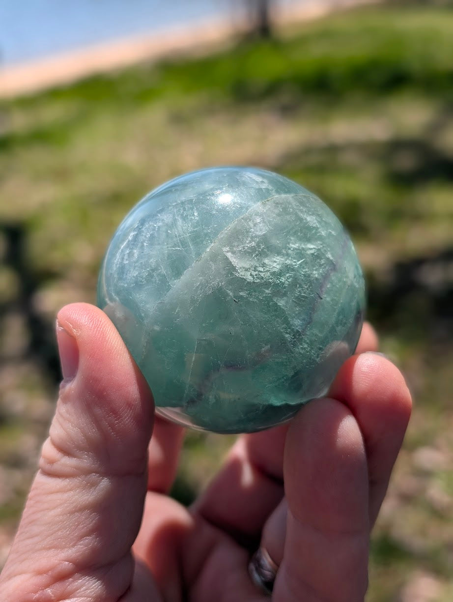 Macro view of a green fluorite sphere held in a hand, emphasizing the natural internal fracture lines and light refraction