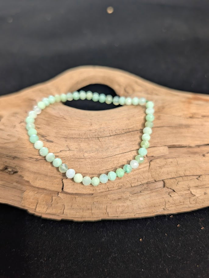 3mm faceted Green Opal beaded stretch bracelet resting on a driftwood display, showing soft mint green colouration.