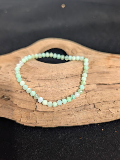 3mm faceted Green Opal beaded stretch bracelet resting on a driftwood display, showing soft mint green colouration.