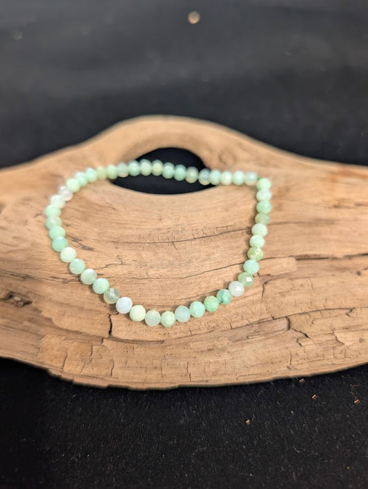 3mm faceted Green Opal beaded stretch bracelet resting on a driftwood display, showing soft mint green colouration.