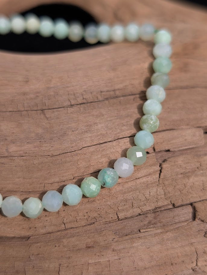 Macro close-up of 3mm faceted Green Opal beads highlighting micro surface cuts and a green stretch cord.