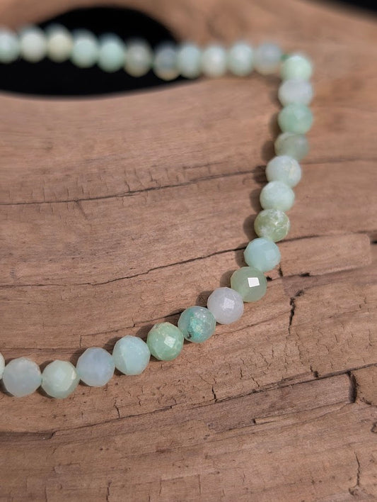 Macro close-up of 3mm faceted Green Opal beads highlighting micro surface cuts and a green stretch cord.
