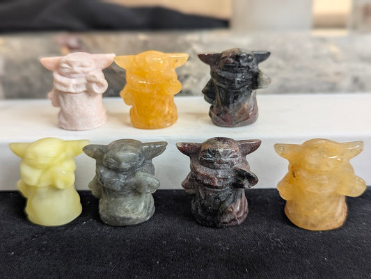 A group of six precision-carved Grogu (Baby Yoda) totems in various natural minerals.