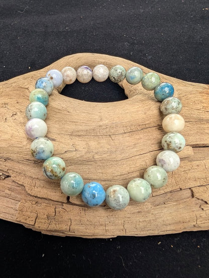 8mm polished Hackmanite beaded stretch bracelet resting on a driftwood display, showing pale grey, blue, and green resting tones.