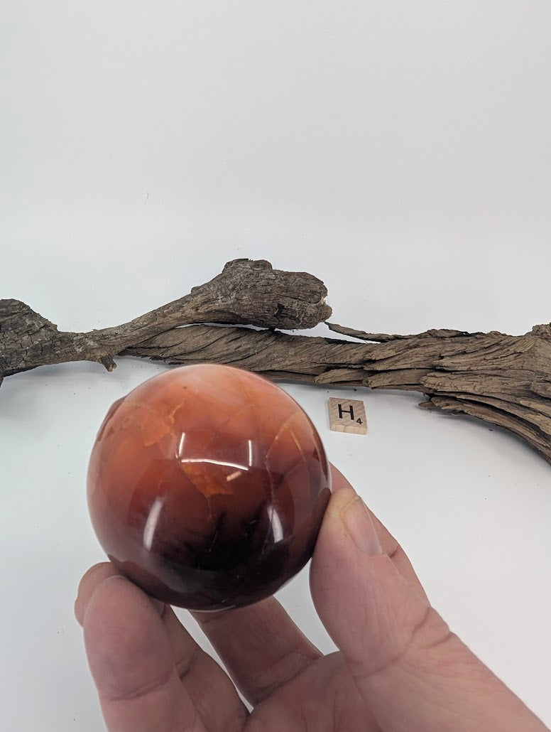 Hand holding a deep red Midnight Mookaite sphere showing opaque polish.