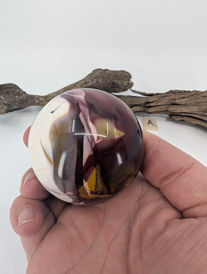 Hand holding a 61mm high-contrast Mookaite sphere to show scale.