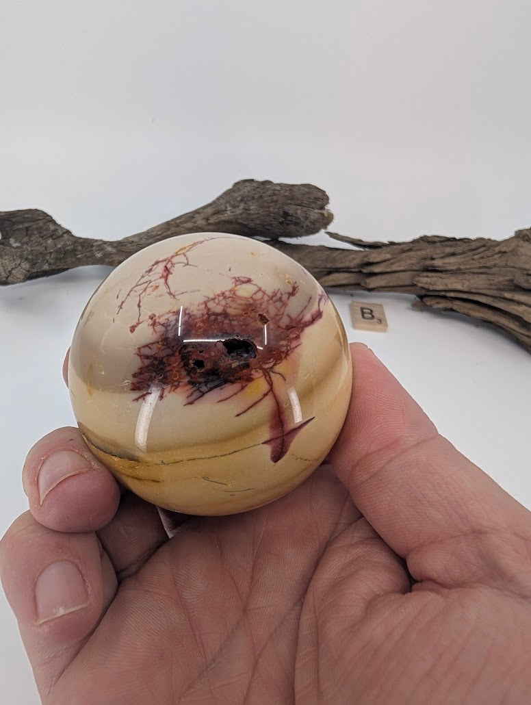 Hand holding a 61mm Mookaite sphere (300g) showing scale.