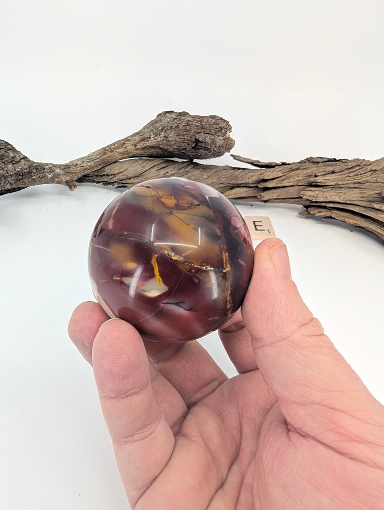 Hand holding a 56mm red Mookaite sphere showing high gloss polish.