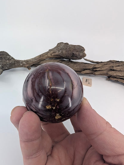 Hand holding a textured Mookaite sphere with purple cracked patterns.
